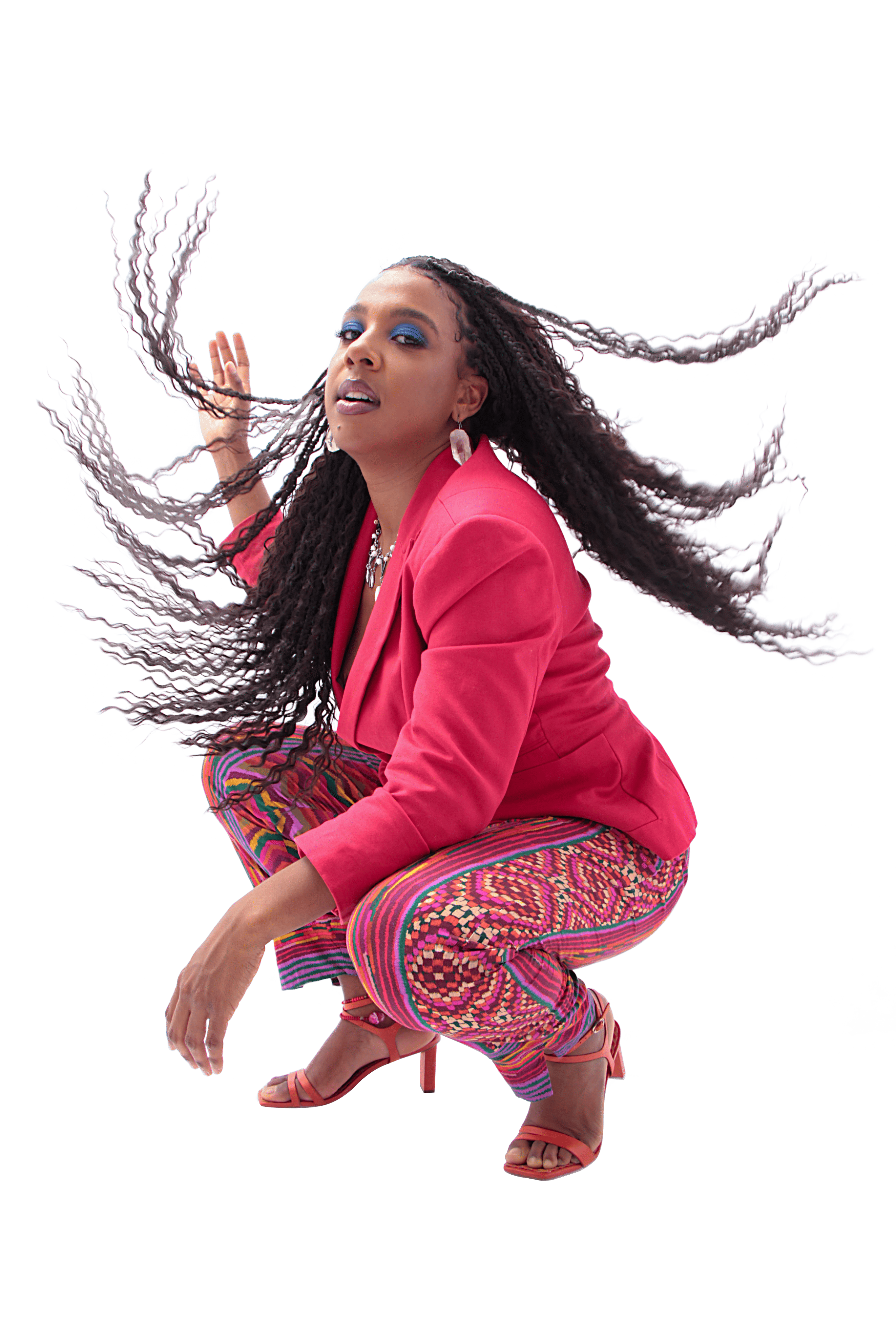 Modelo negra agachada com blazer rosa e cabelos trançados ao vento